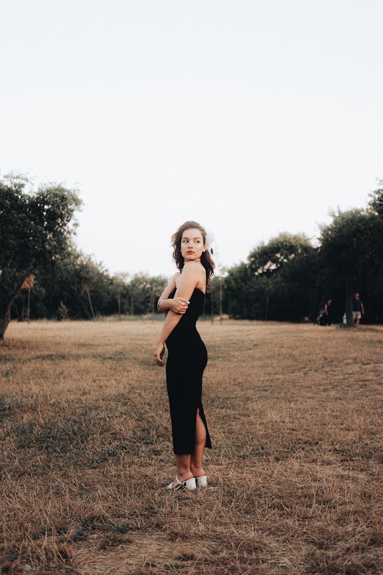 Young Woman In Black Bandeau Maxi Dress And White Shoes Standing On A Lawn