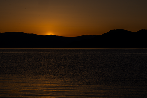 Free Peaceful sunset with silhouetted mountains and calm lake waters. Stock Photo