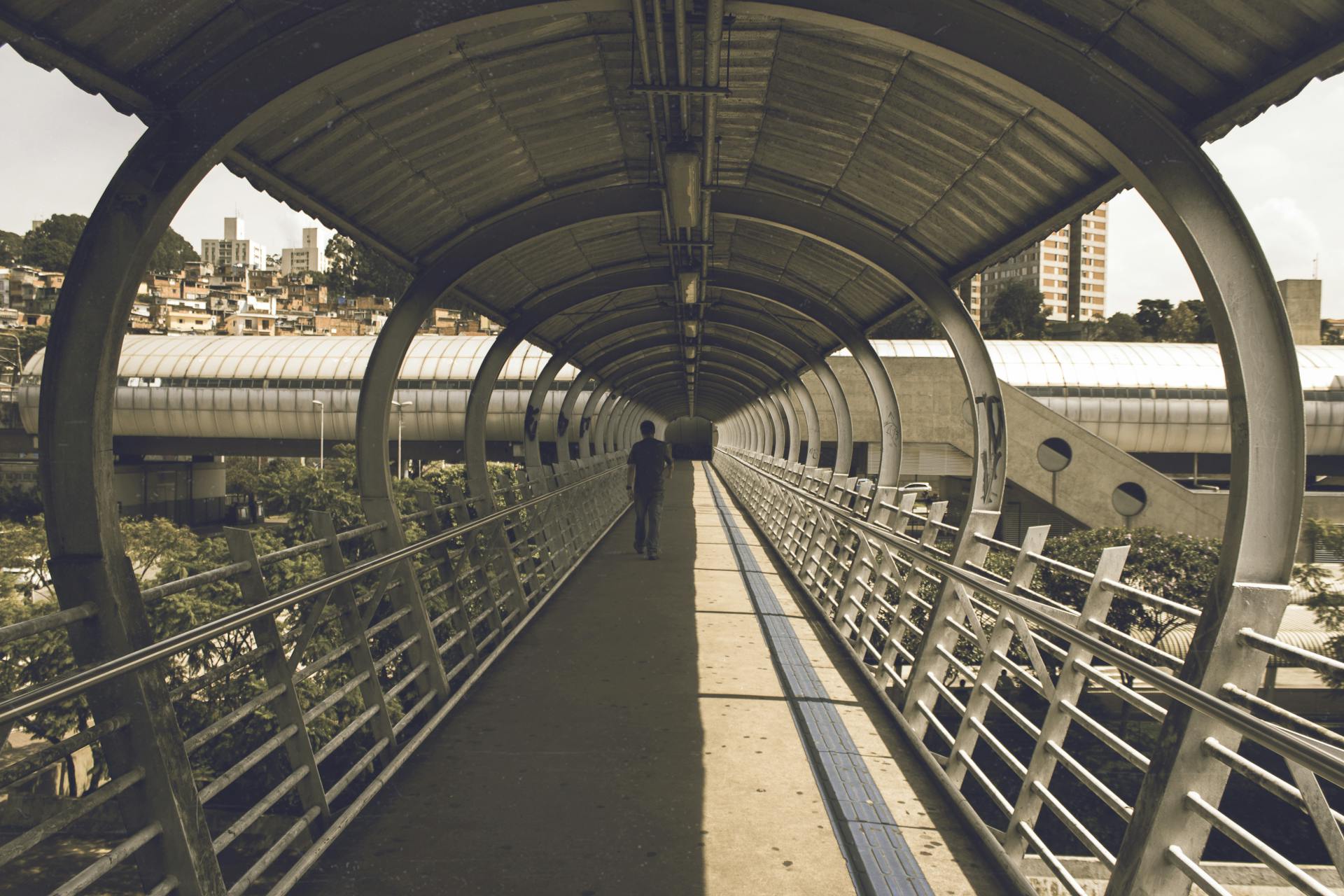 A person walking on a modern urban footbridge with curved architecture in daylight.