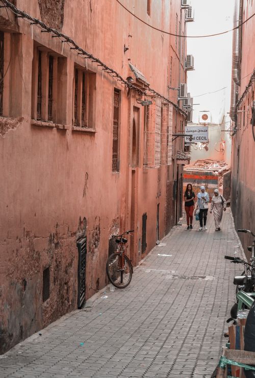 Free Explore a narrow alley in Morocco featuring vintage buildings, a bicycle, and strolling locals. Stock Photo