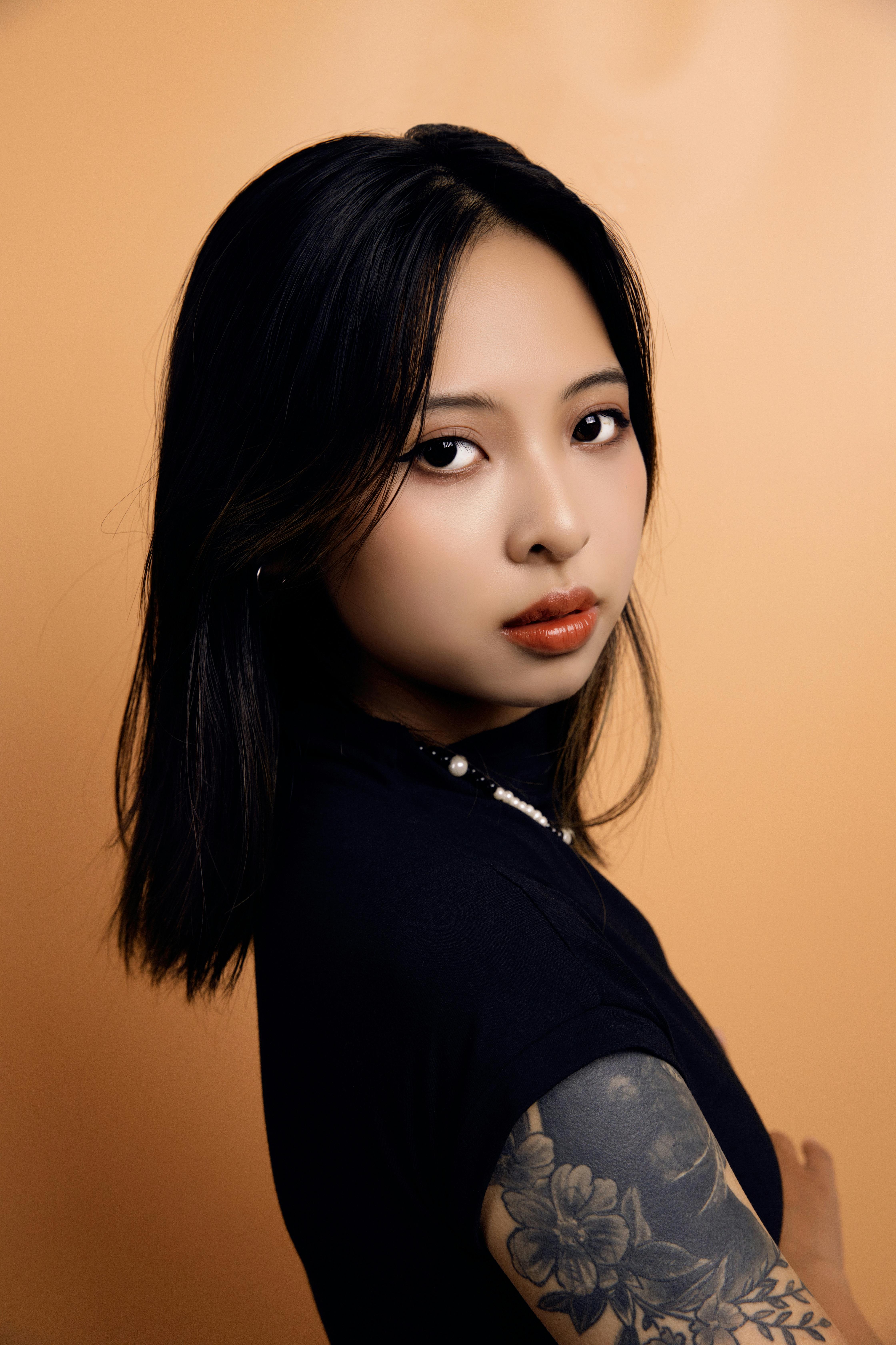 Elegant portrait of a young woman with expressive eyes and floral tattoos, posing against a warm background.