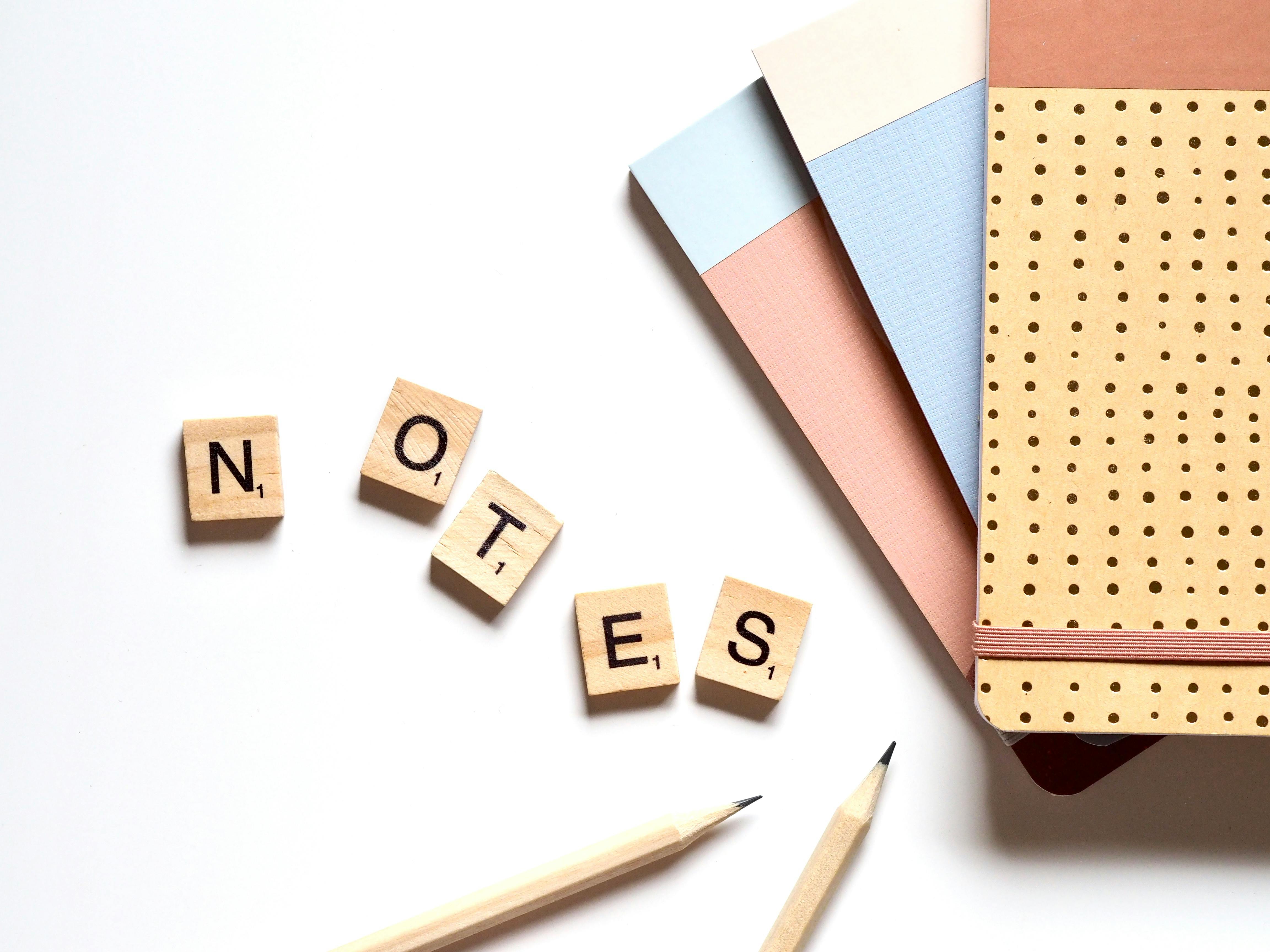 five brown wooden scrabble tiles beside two pencils