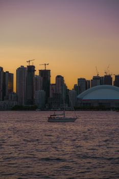 A stunning view of the Toronto skyline at sunset with a sailboat on the water.