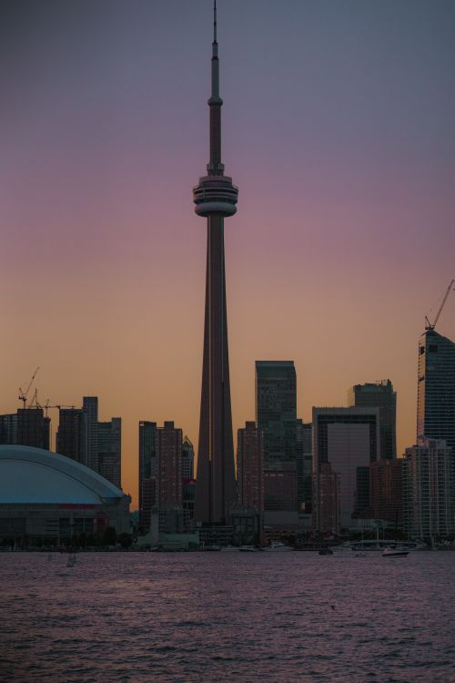 Free Majestic CN Tower stands tall amidst Toronto's cityscape at sunset, reflecting over calm waters. Stock Photo