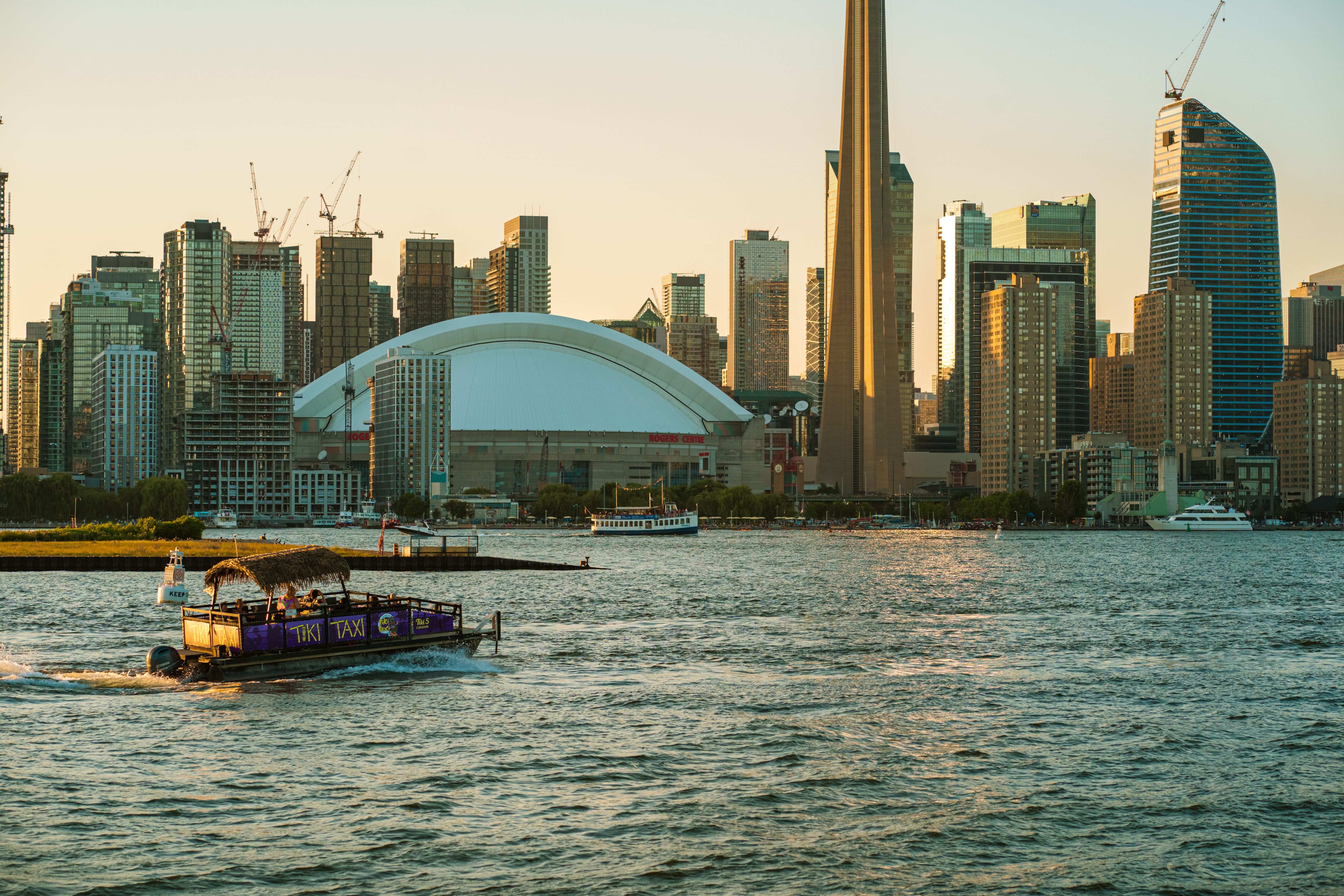 Scenic view of Toronto's skyline and waterfront at sunset featuring the iconic CN Tower and a passing boat.