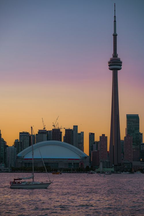 Free Capture of Toronto's skyline at sunset, featuring the CN Tower and a sailboat on Lake Ontario. Stock Photo