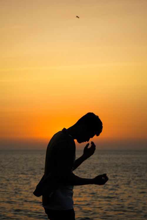 Free A silhouetted man stands contemplatively by the sea during a vibrant sunset in Mumbai, India. Stock Photo