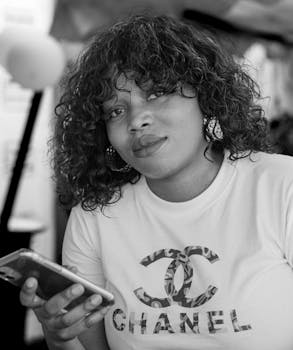 Stylish young woman with curly hair holding a phone. Black and white portrait.