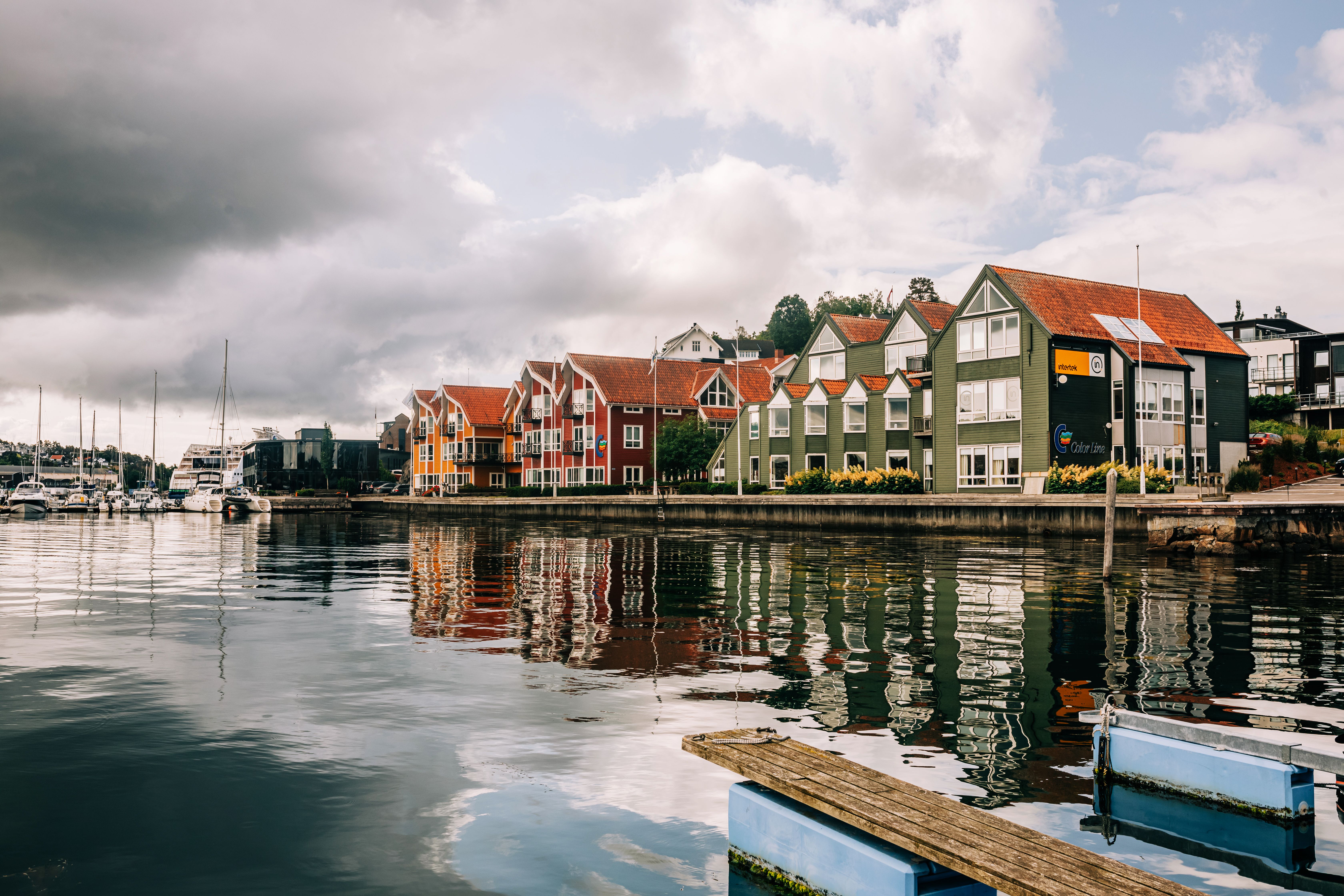 Charming waterfront town with colorful houses reflecting on calm waters under a cloudy sky.