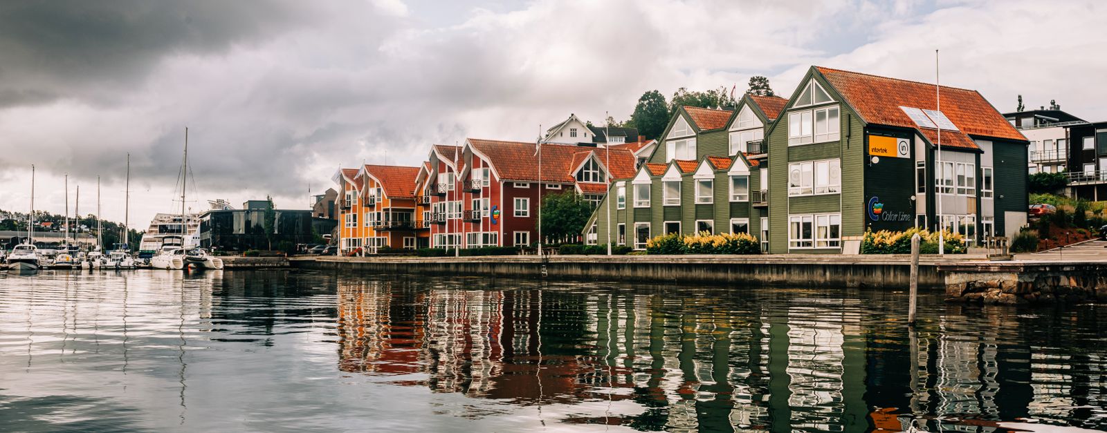 Charming waterfront town with colorful houses reflecting on calm waters under a cloudy sky.