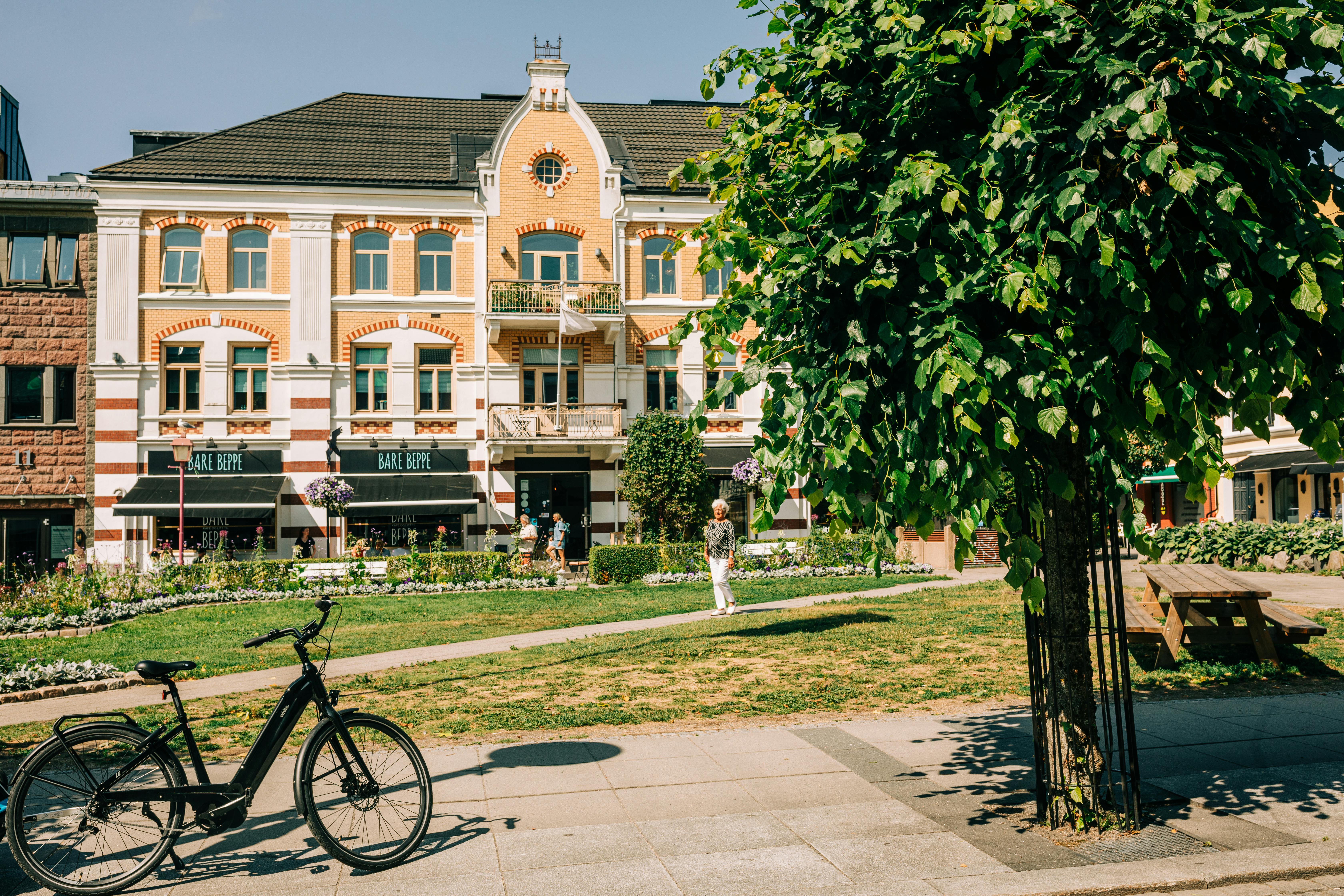 Explore a sunny day in Sandefjord with a picturesque building, lush greenery, and vibrant urban life.