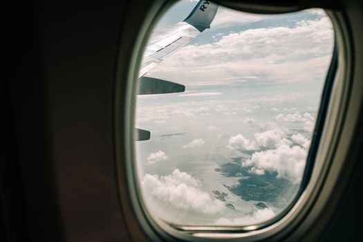 View through airplane window showing wing and ocean with clouds below during daylight flight.