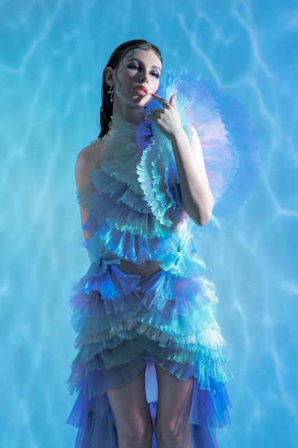 Striking portrait of a woman posing in a layered blue iridescent dress against a matching background.