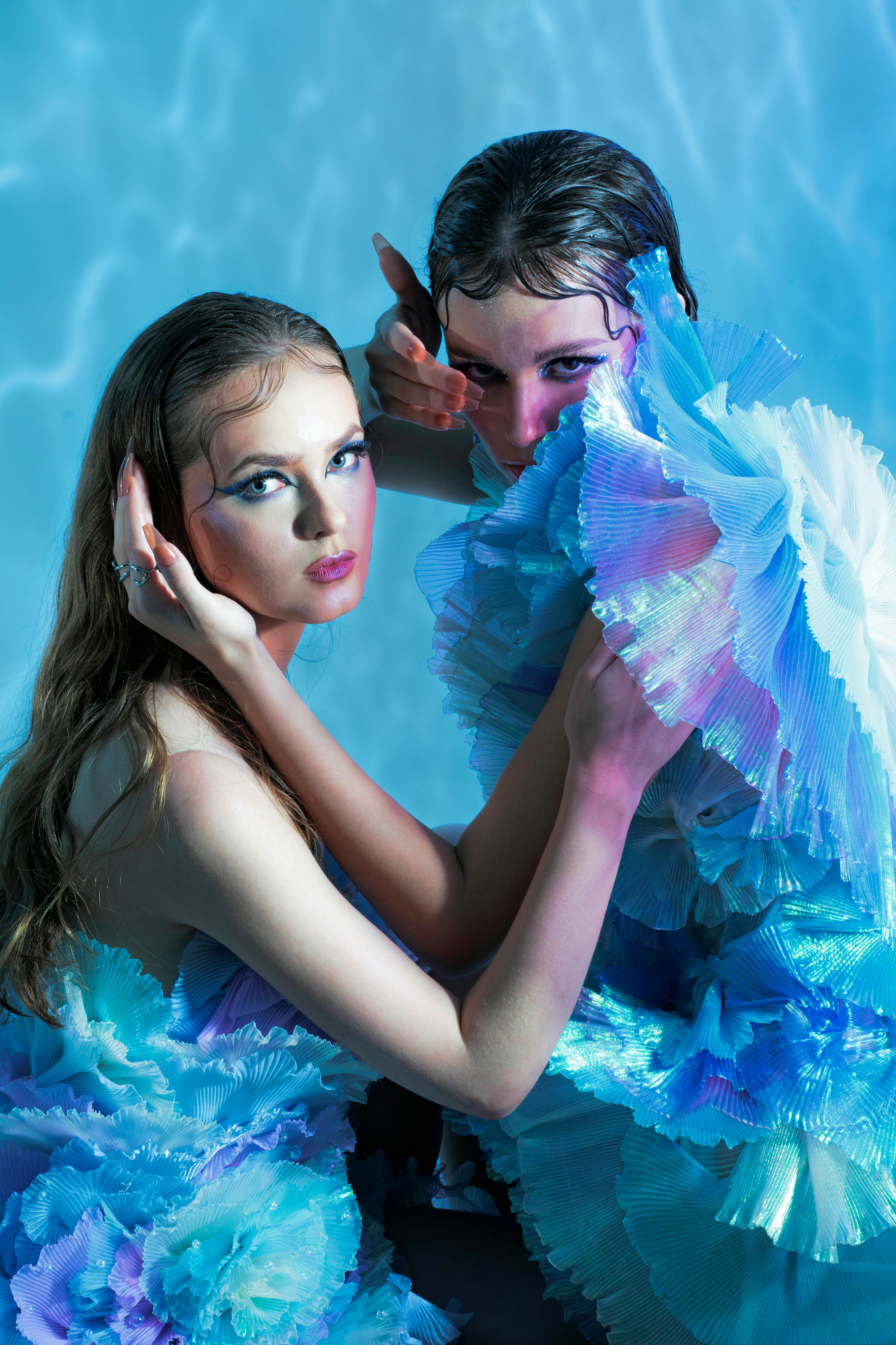 Artistic portrait of two women in blue ruffled dresses posing with water-like background.