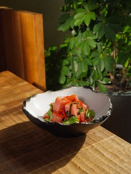 Close-up of a fresh salmon salad served in an artisanal ceramic bowl on a wooden table.