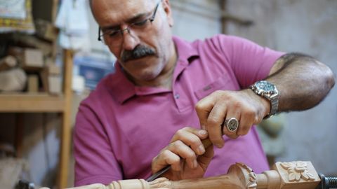 Elderly craftsman focused on intricate woodwork in a traditional workshop.