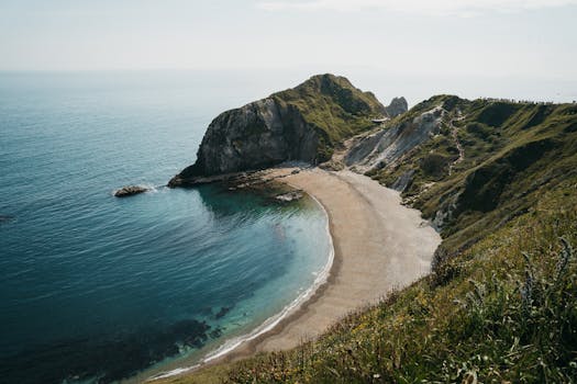 Beautiful coastal scene featuring a serene beach cove with lush cliffs and clear blue sea under the daytime sky.