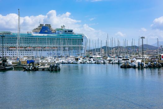 Large cruise ship docked at Ajaccio marina, surrounded by yachts on a sunny day.