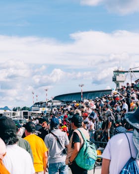 A large diverse crowd views an event on an airport tarmac under a clear sky.