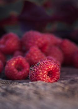 Detailed shot of ripe red raspberries lying on a wooden surface, emitting a fresh and juicy appeal.