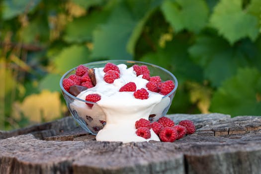 A delicious raspberry dessert with cream on a wooden stump, surrounded by lush greenery, embodying a summer vibe.