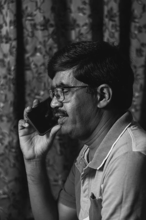 Free Black and white portrait of an adult man using a smartphone indoors, wearing glasses. Stock Photo