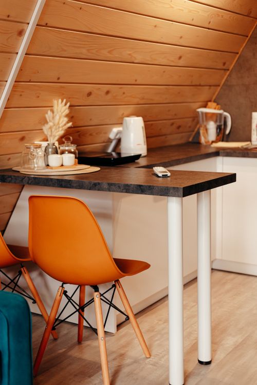 Free Warm and inviting modern kitchen with slanted wood ceiling, orange chairs, and countertop appliances. Stock Photo