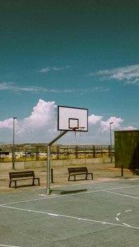 Sunlit urban basketball court in Madrid, España with benches and clear sky backdrop.