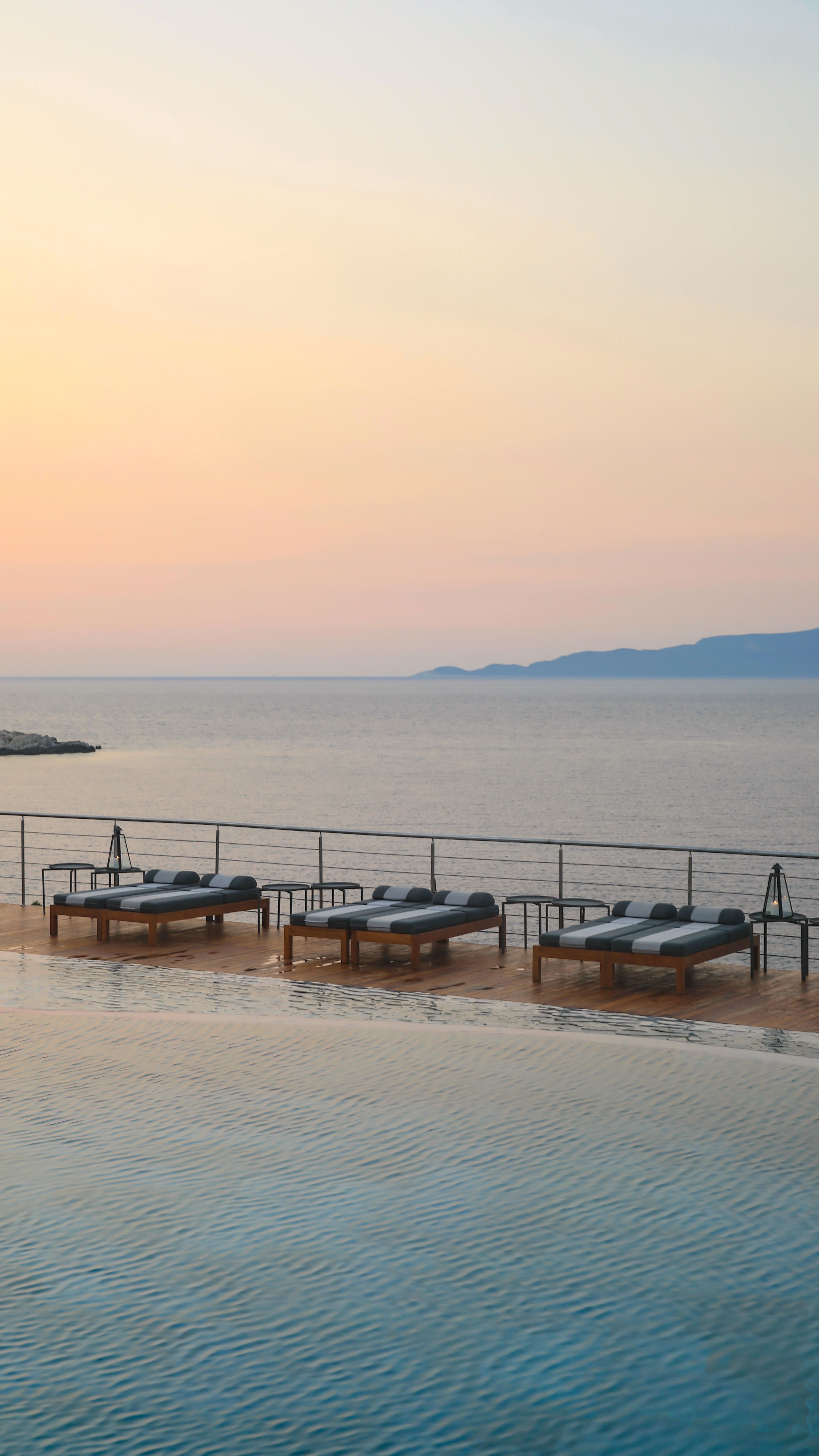 Tranquil coastal resort with sunbeds and infinity pool, overlooking a calming ocean at sunset.
