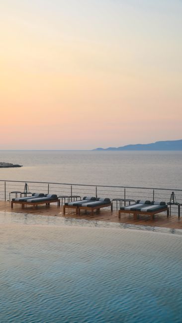 Tranquil coastal resort with sunbeds and infinity pool, overlooking a calming ocean at sunset.