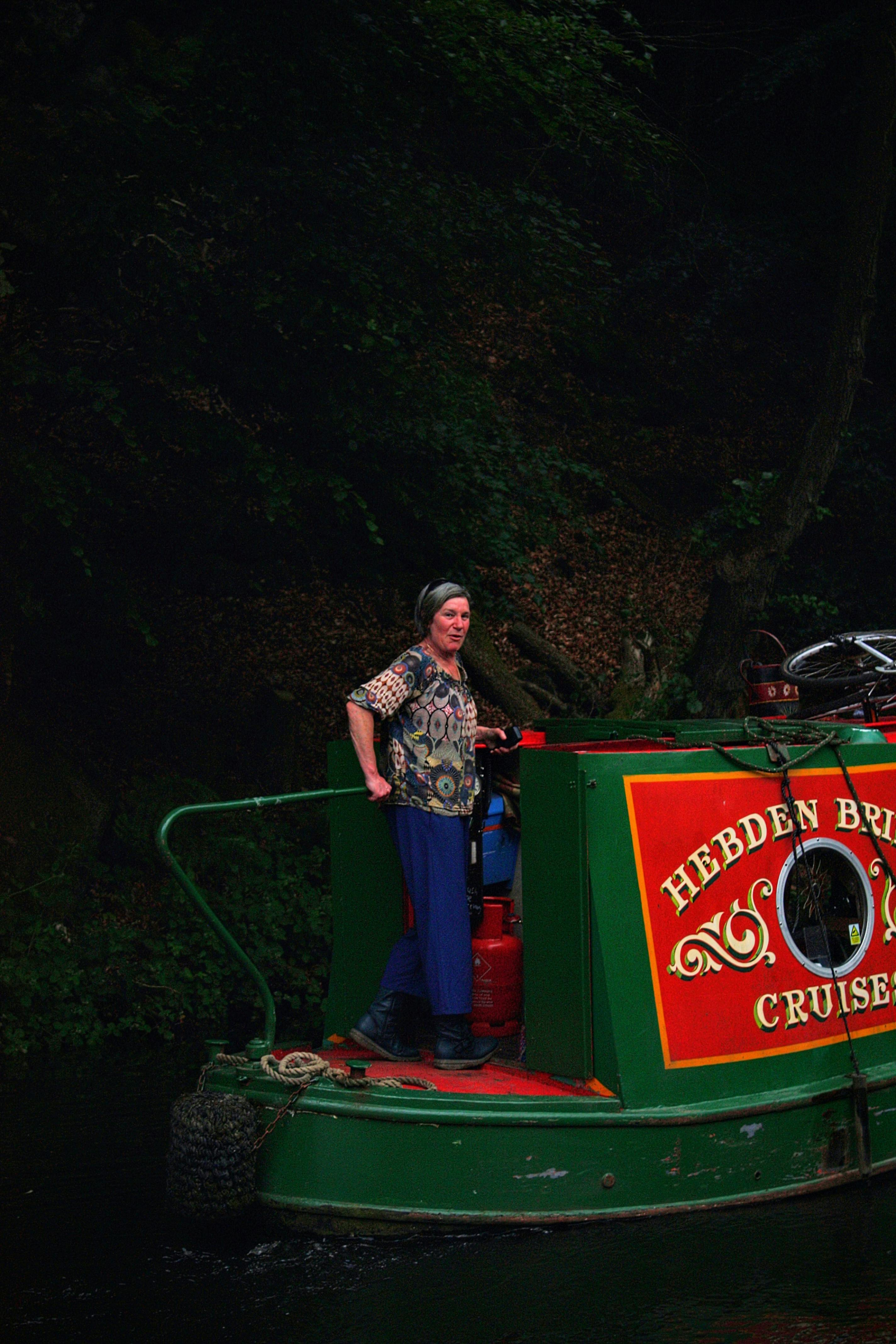 Woman on a colorful narrowboat in Hebden Bridge, England, enjoying a scenic cruise.