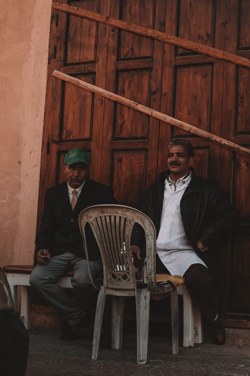 Free Two elderly men sit on a bench in an urban area, framed by wooden doors, creating a classic and warm atmosphere. Stock Photo
