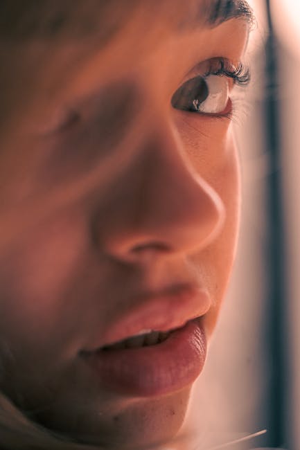 Intimate close-up of a young person's face highlighting an eye and lips in warm tones.