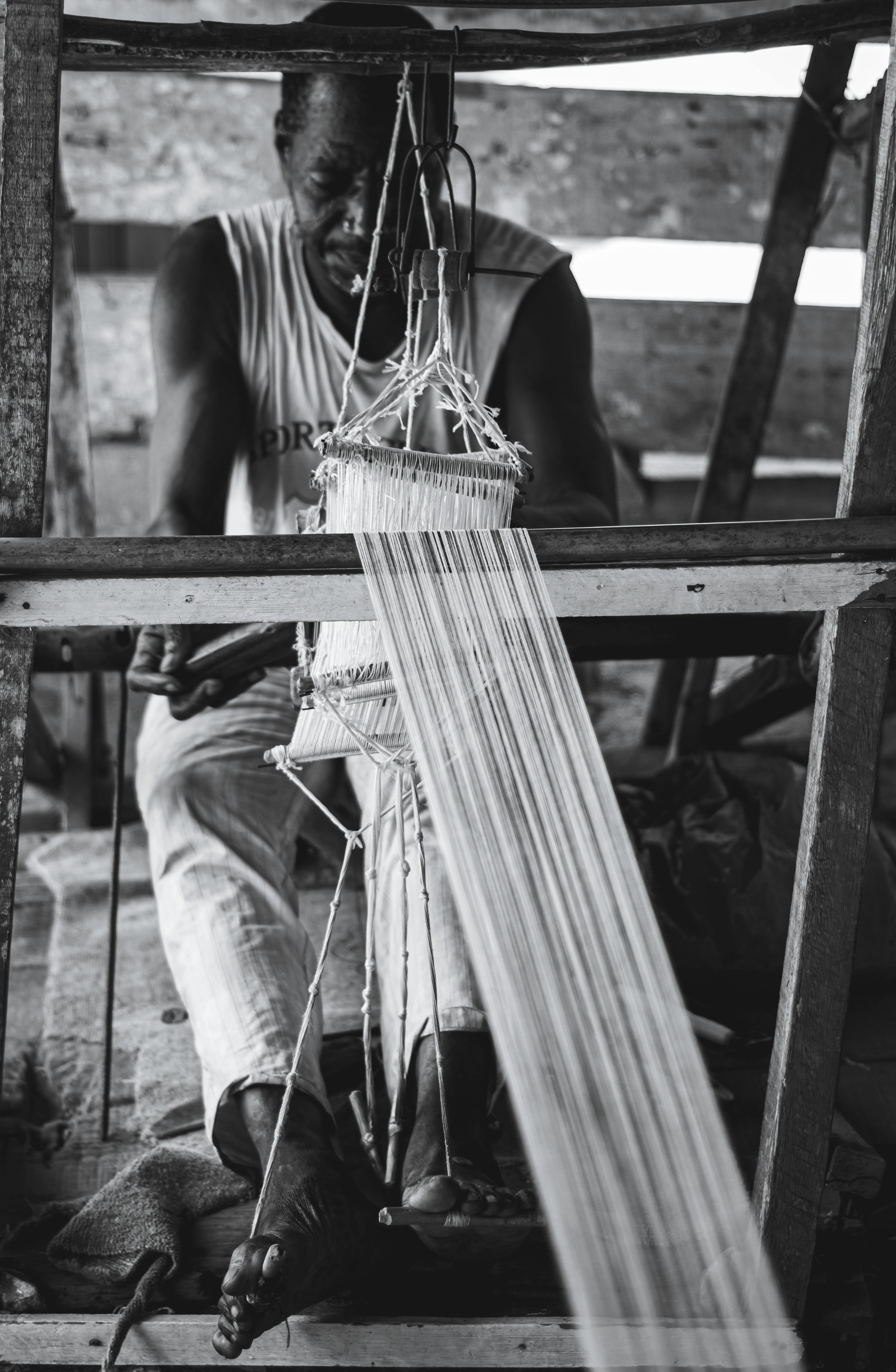 A skilled artisan focused on weaving fabric on a traditional loom, captured in monochrome.