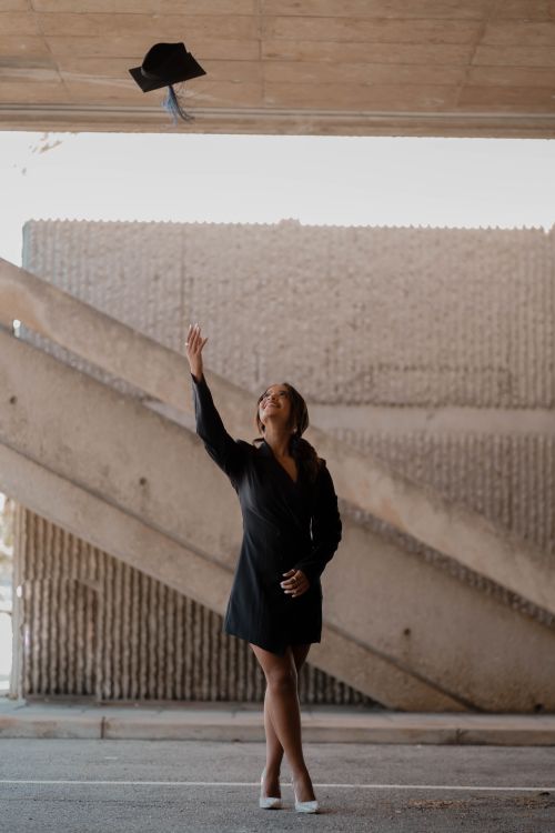 Free A young woman joyfully tosses her graduation cap indoors, celebrating her academic achievement. Stock Photo