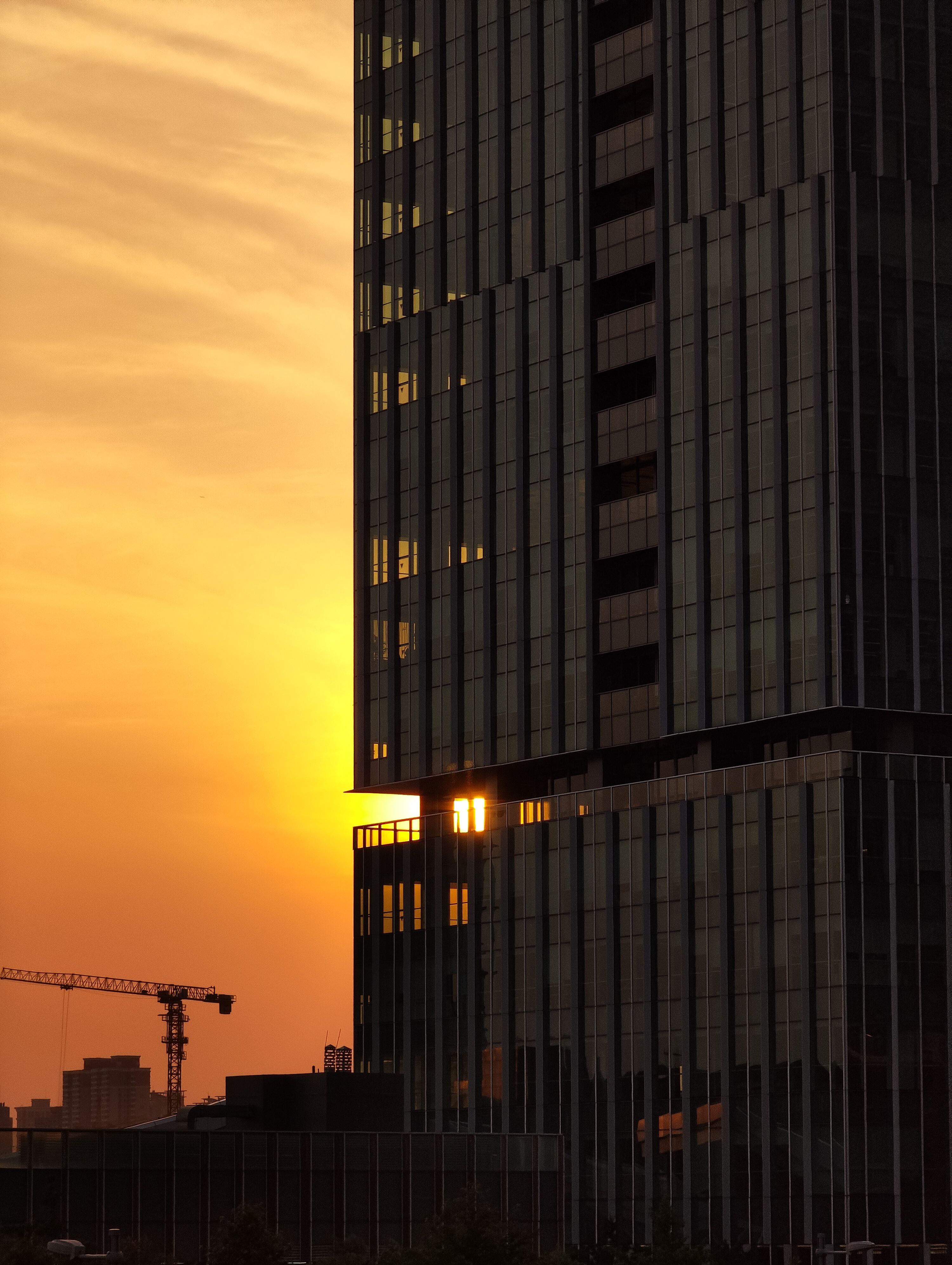 Sunset view of a Shanghai skyscraper and crane against a vibrant sky.