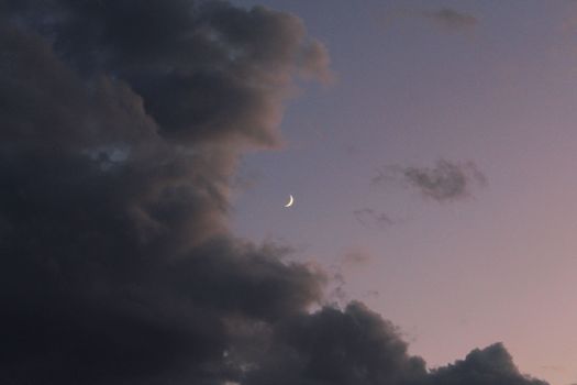 A stunning crescent moon hangs amidst dramatic clouds in the evening sky over Sinop, Türkiye.