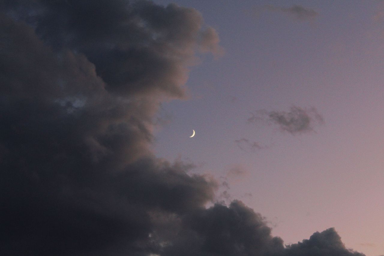 a stunning crescent moon hangs amidst dramatic clouds in the evening s