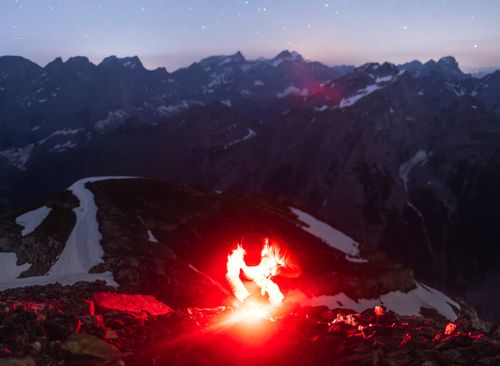 Free Hiker lit by flare in the mountainous terrain under a starry sky. Stock Photo