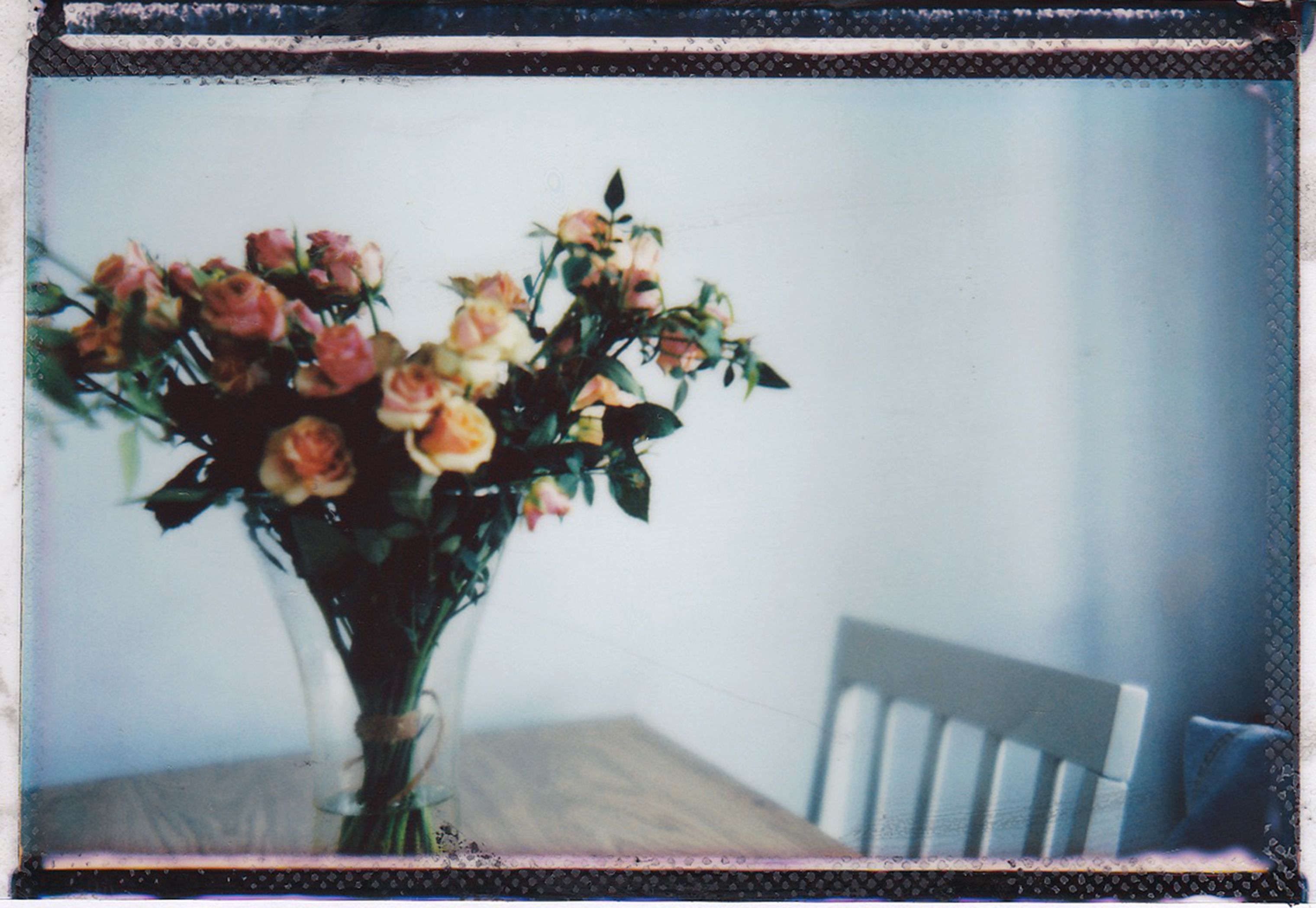 Artistic photo of a rose bouquet in a glass vase on a table, exuding a vintage vibe.