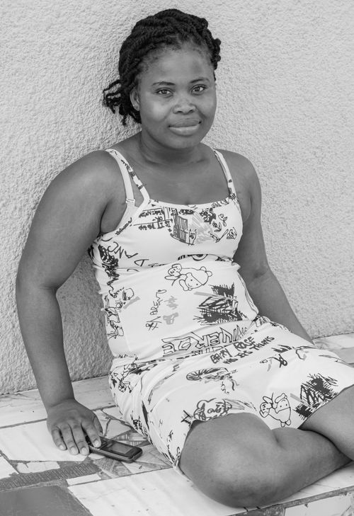 Free Black and white portrait of a smiling woman sitting against a wall, holding a phone. Stock Photo