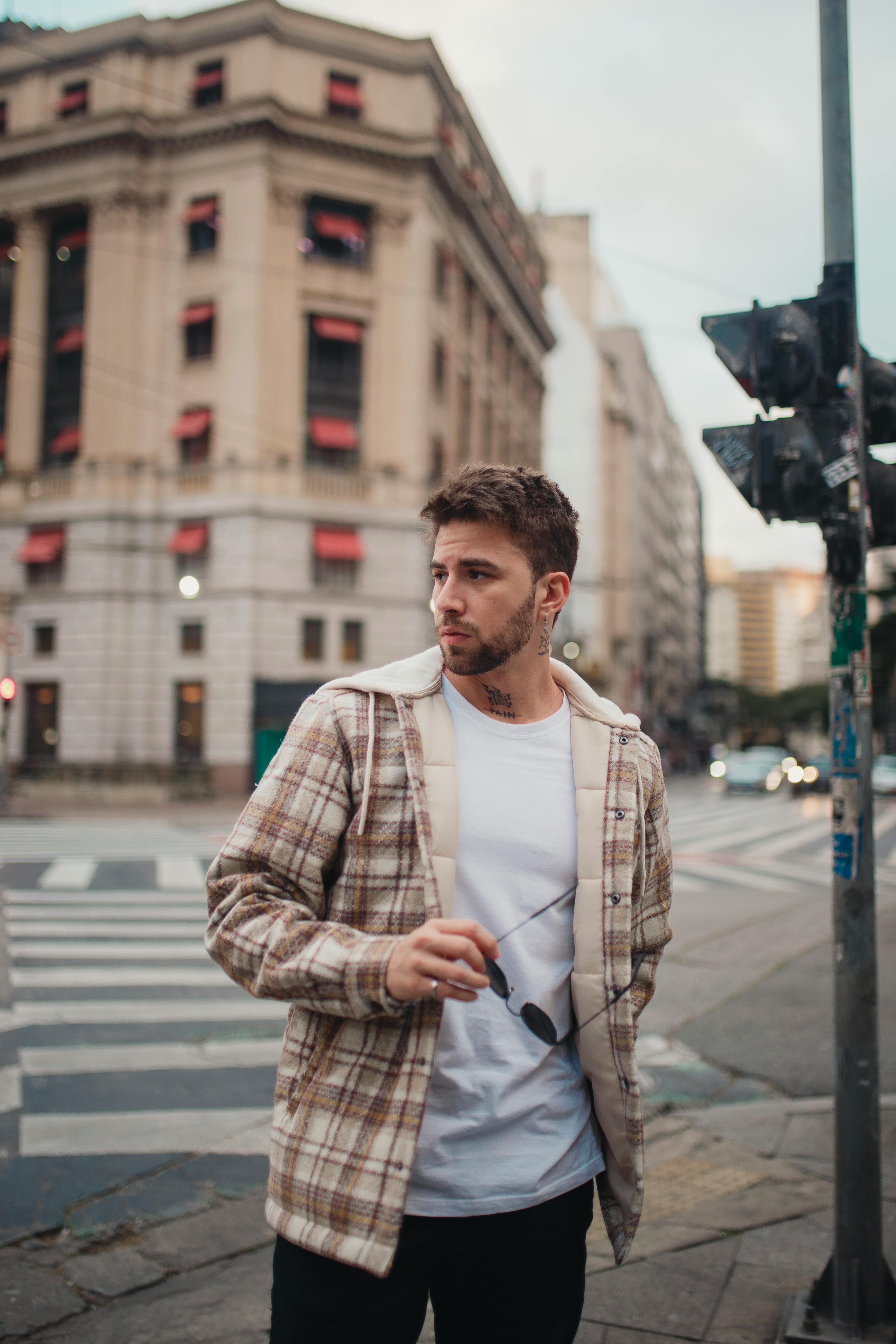 Stylish man poses on city street, embodying urban fashion with a plaid jacket.