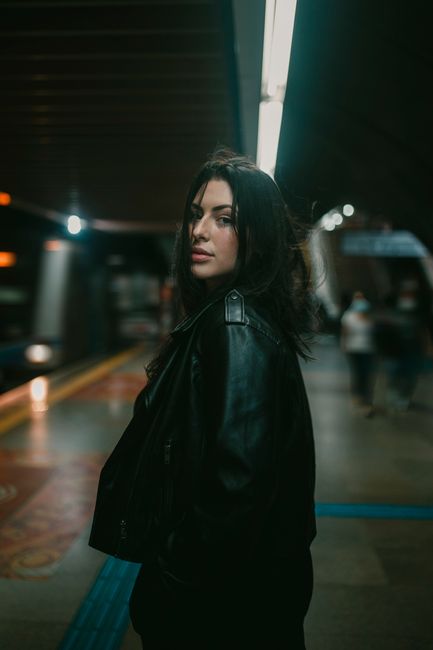 A woman in a leather jacket looks over her shoulder in a dimly lit subway station.