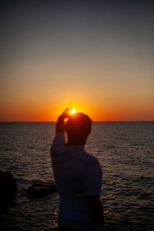 Man Catching Sun at Sunset on Sea Shore 