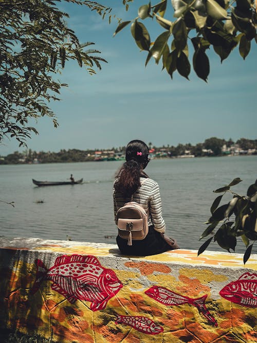 Woman with Backpack Sitting on Painted Wall near River