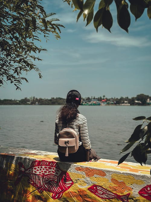 Woman with Backpack Sitting on Wall by River