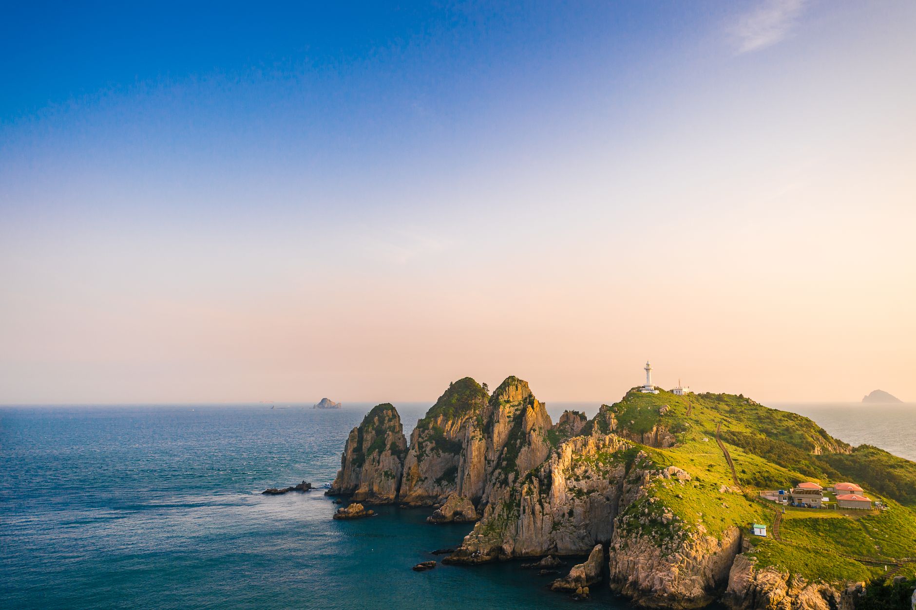 Beautiful aerial view of an island with a lighthouse during sunset, surrounded by the ocean.