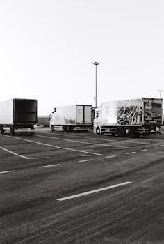 Black and white photo of multiple trucks parked in an empty urban parking lot, taken during the day.