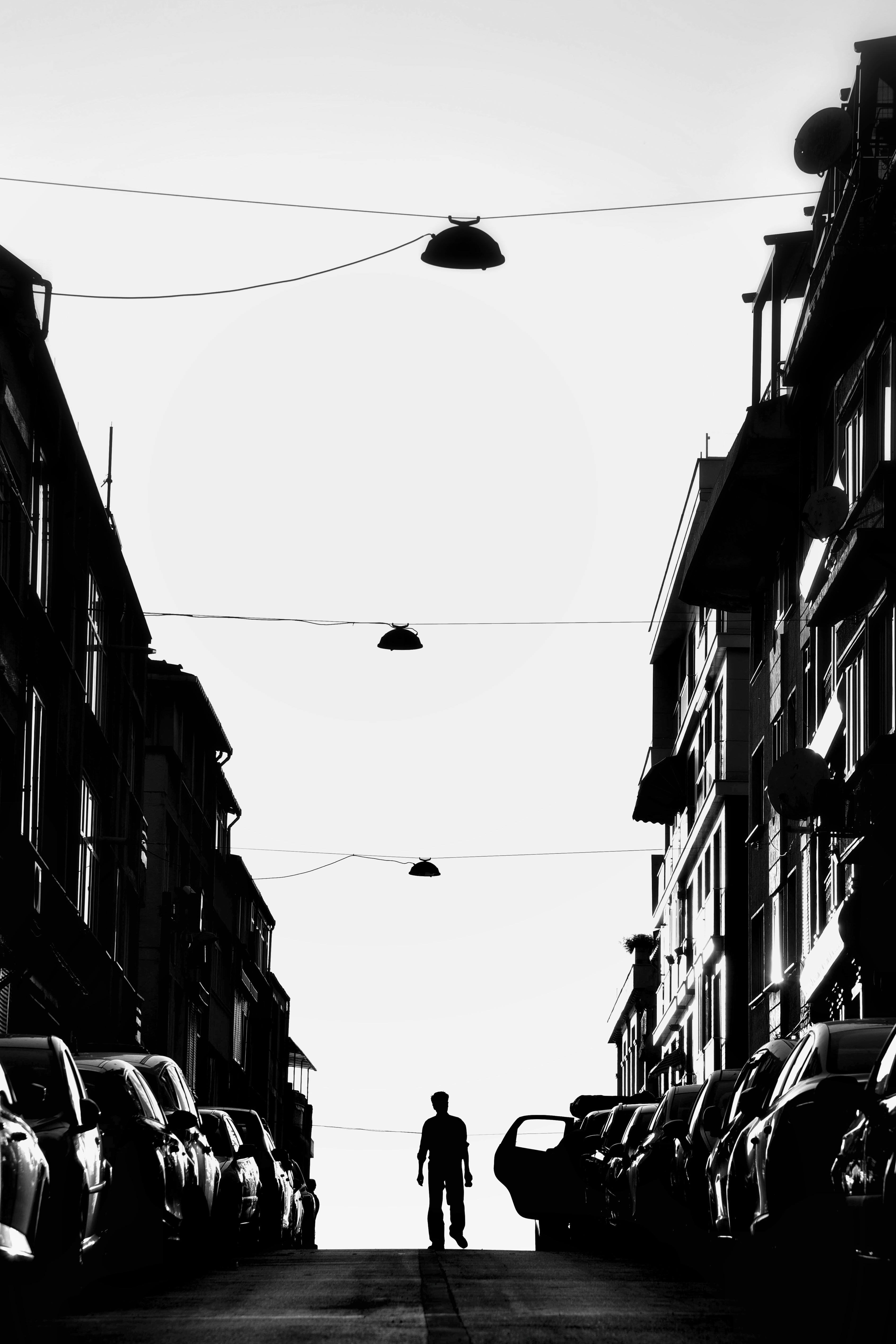 Black and white photo of a man walking on a car-lined city street, capturing urban lifestyle.