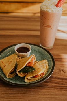 A mouthwatering meal featuring savory crepes with a refreshing fruit smoothie on a wooden table.